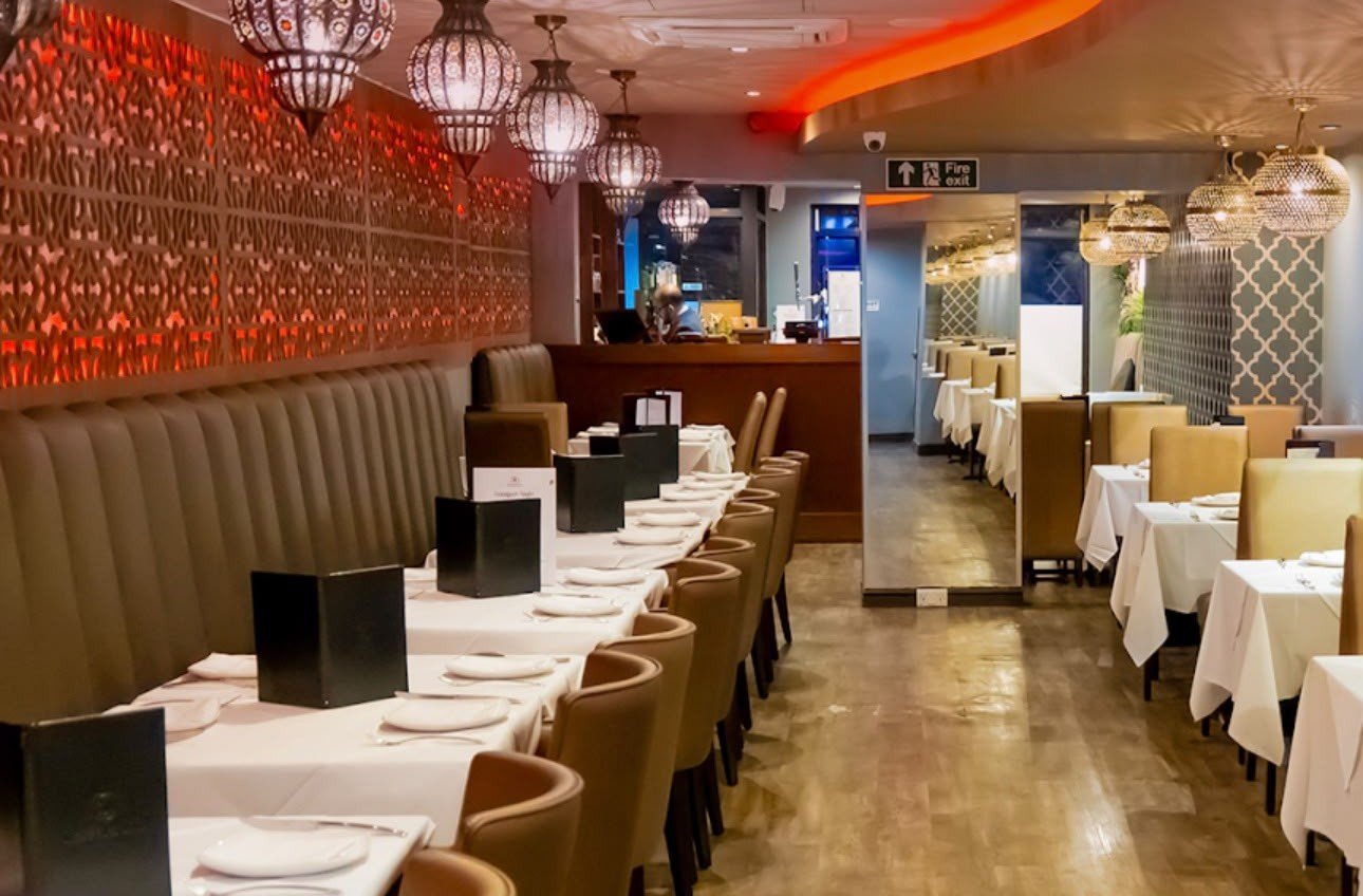 The dining room at Masala Inn: a long banquette beside a red patterned wall, hanging lanterns and tables laid with white cloths